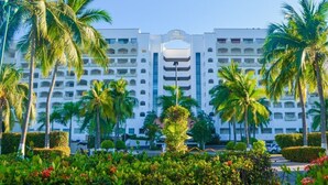 A multi-story hotel with a central entrance, surrounded by palm trees and well-maintained gardens. - Condominio 02 recamaras Enna Inn Ixtapa (Ixtapa)