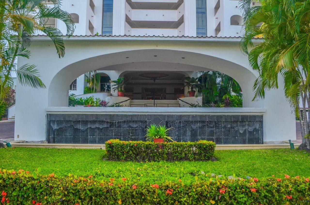 A building with a central courtyard, surrounded by lush greenery and palm trees.