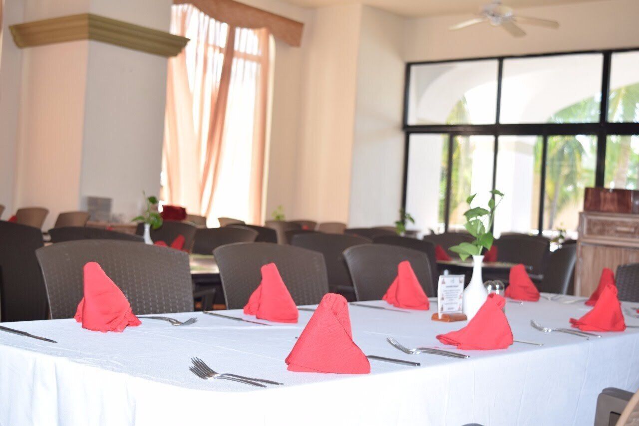 A dining area with tables set for service, featuring red napkins and white tablecloths.