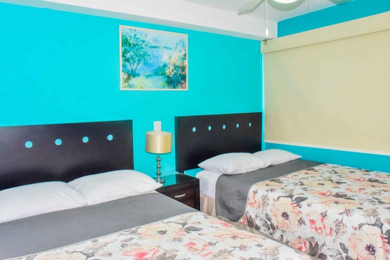 A room with two beds, a painting on the wall, and a window with blinds.