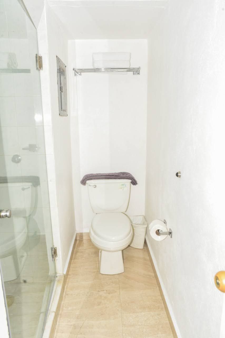 Un baño pequeño y funcional con inodoro, cabina de ducha de vidrio y suelo de baldosas blancas.