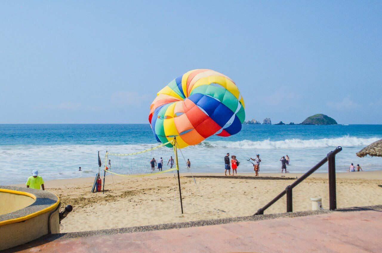 A beach with a colorful parasail, a volleyball net, and people in the background.