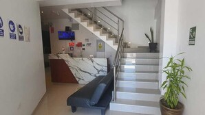 A modern hotel lobby with a marble reception desk, a staircase, a sofa, and a potted plant. - Hotel Golden Sky (Pariñas)