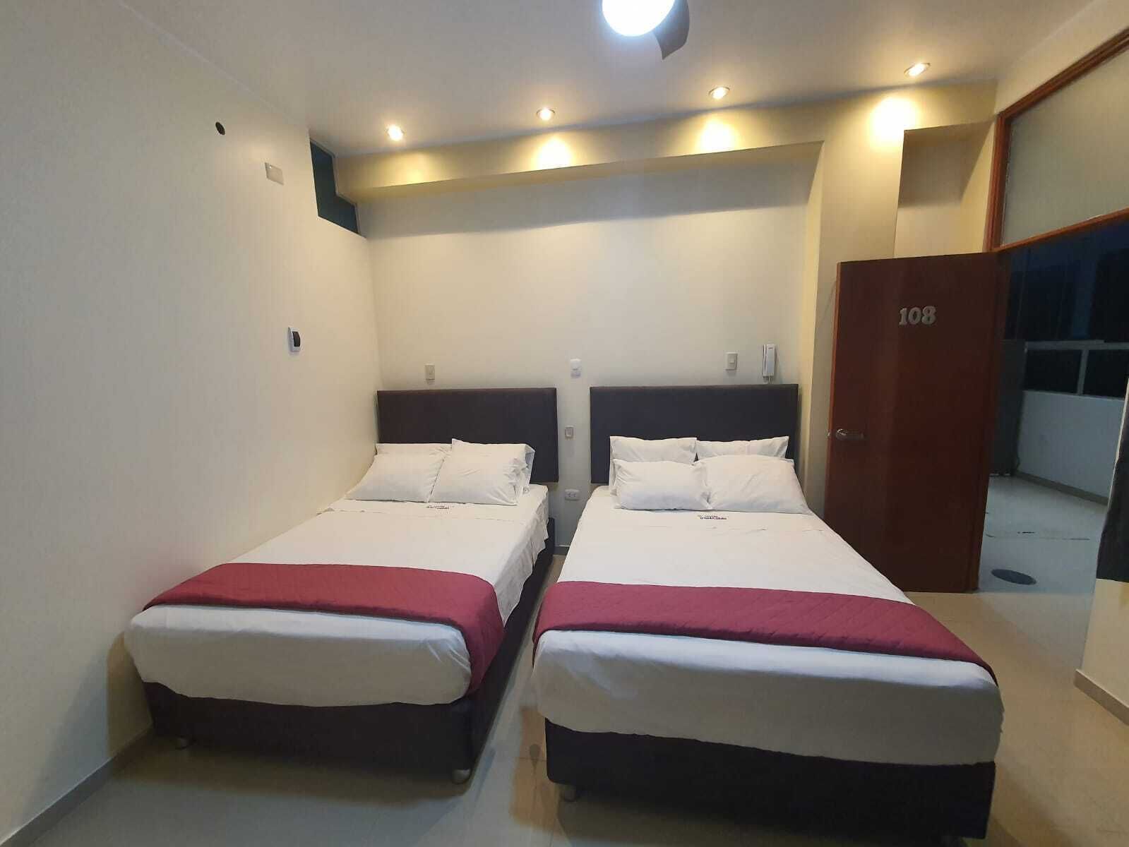 A hotel room with two single beds, a wooden door, and a small window.