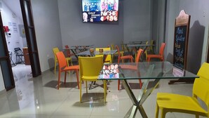 A dining area with a glass table and yellow chairs, a television screen above, and a chalkboard menu on the wall. - Hotel Golden Sky (Pariñas)