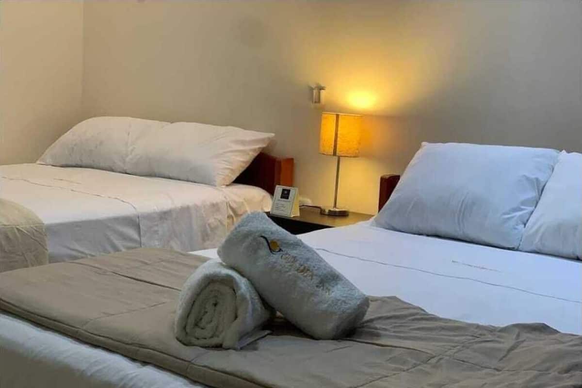 A hotel room with two beds, a nightstand with a lamp, and a rolled towel on the bed.