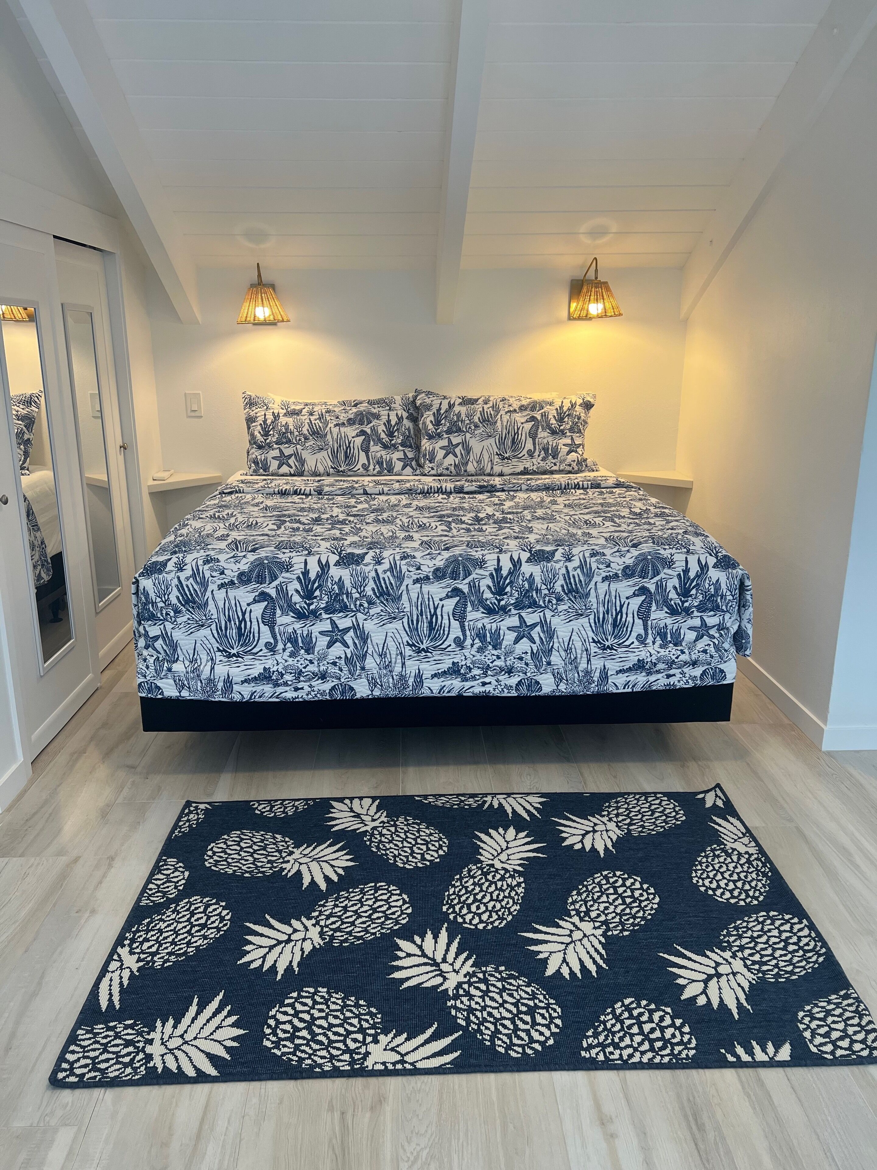 Ein Schlafzimmer mit einem Bett, zwei Nachttischlampen und einem dunkelblauen Teppich mit Ananas-Muster.