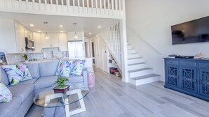 A modern living room with a grey sofa, a glass coffee table, and a staircase leading to an upper level. - Aloha Maui Condos (Lahaina)