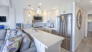 A modern kitchen with white cabinetry, stainless steel appliances, and a central island. - Aloha Maui Condos (Lahaina)