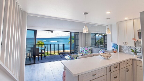 A modern kitchen with a large island, white cabinets, and a view of the ocean. - Aloha Maui Condos (Lahaina)