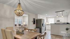 Cozinha moderna com armários brancos, uma ilha central e uma área de refeições com mesa e cadeiras de madeira.