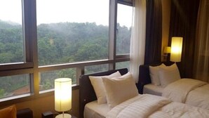 Habitación de hotel con dos camas, una mesita de noche, una lámpara y vistas a una zona boscosa.