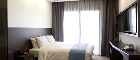 Habitación de hotel con una cama grande, un escritorio con teléfono, televisión y ventana con cortinas.