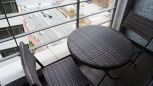 Un balcón con mobiliario de mimbre, vista a una calle de la ciudad y un edificio con fachada de vidrio.