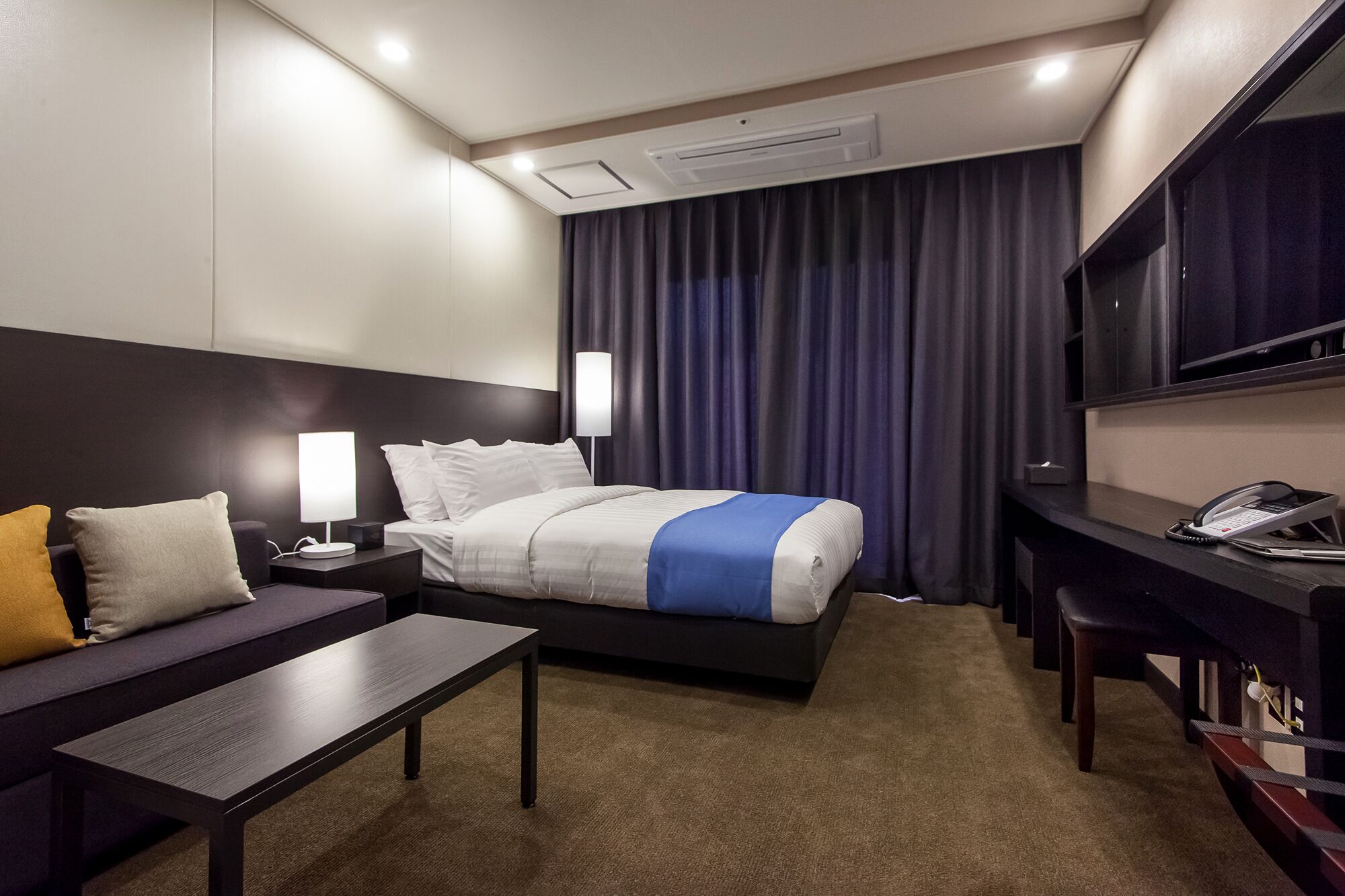 A hotel room with a bed, bedside tables, a desk, a chair, a TV, and a phone.