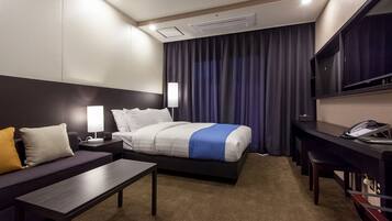 A hotel room with a bed, bedside tables, a desk, a chair, a TV, and a phone.