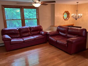 Une pièce avec deux canapés en cuir rouge, un plancher en bois, un ventilateur de plafond, un vitrail et un lustre.