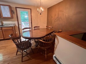 Un coin repas avec une grande table en bois et quatre chaises. Un lustre est suspendu au plafond.