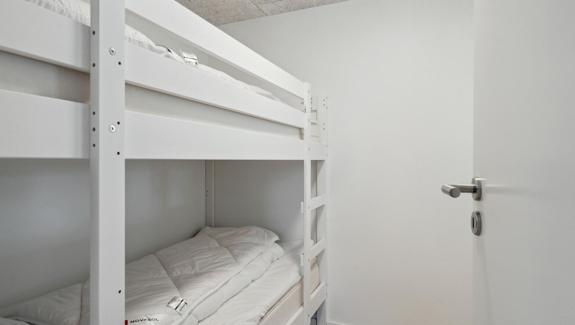 Een stapelbed met een deur aan de rechterkant, een witte muur en een metalen handgreep.