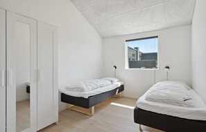 Ein kleines, modernes Schlafzimmer mit zwei Einzelbetten, einem Kleiderschrank und einem Fenster mit Blick hinaus.