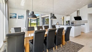 A modern kitchen with a central island, a dining area with a wooden table and black chairs, and large windows offering a view of the outdoors. - Stunning home in Tarm with kitchen (Tarm)