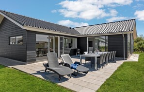 Ein modernes Haus mit einer Terrassenfläche, ausgestattet mit Gartenmöbeln und einem Esstisch.