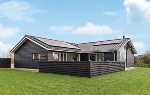 Ein modernes, zweistöckiges Haus mit dunkler Fassade, großen Fenstern und einem geneigten Dach.