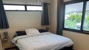 A bedroom with a bed, a window with curtains, an air conditioning unit, and a lamp. - Beach side duplex (punaauia)
