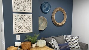 A modern kitchen with a wooden countertop, a grey sofa, decorative wall art, and a patterned rug.