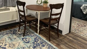 A small room with a round wooden table, two chairs, a television mounted on the wall, a small clock, and a potted plant.