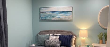 Een slaapkamer met een bed, nachtkastje, lamp, spiegel en een schilderij aan de muur.