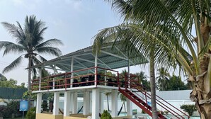 A two-story building with a covered terrace, palm trees, and a staircase leading to the upper level.