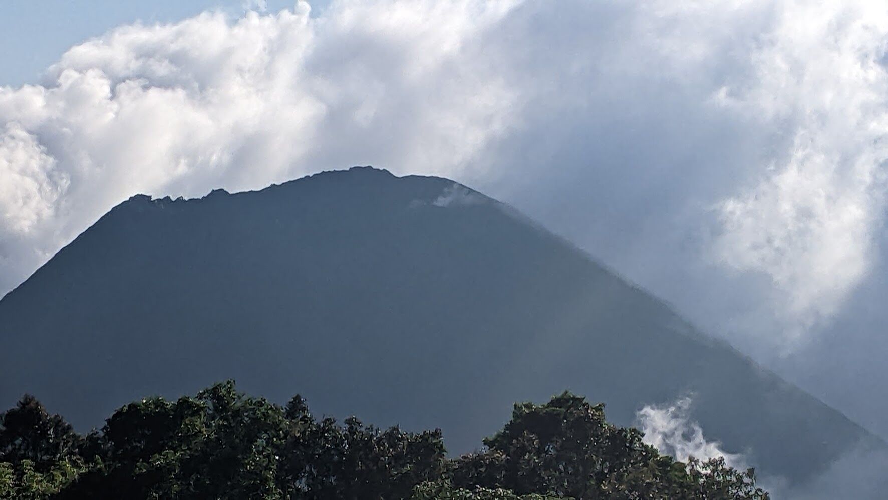Une montagne dont le versant inférieur est couvert de forêt et dont le sommet est entouré de nuages.