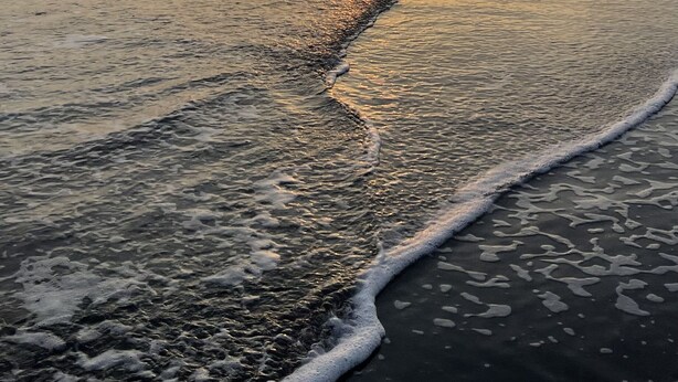 A beach at sunset with waves, a clear sky, and a distant horizon.