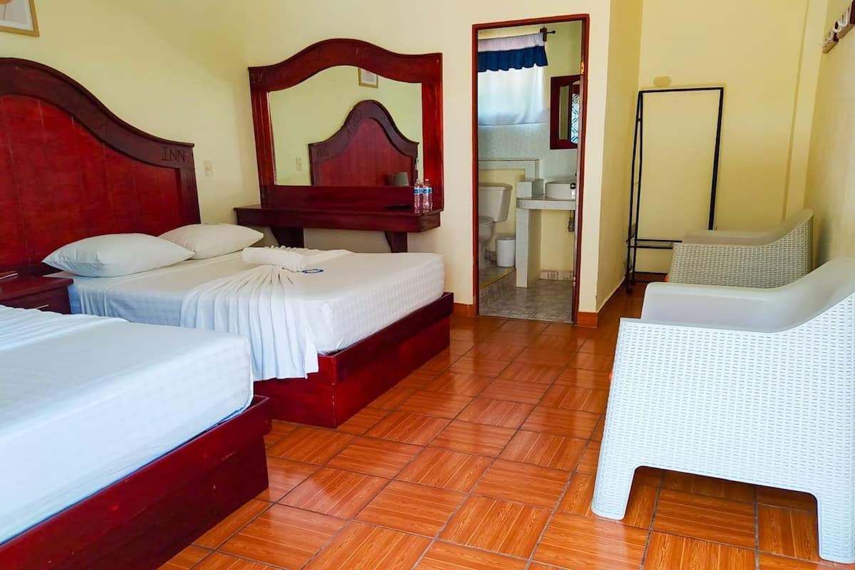 Une chambre d’hôtel avec deux lits, une salle de bain et une chaise blanche.