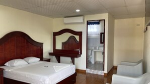 A bedroom with a wooden bed, a nightstand, a dresser, a mirror, and a bathroom visible through an open door.