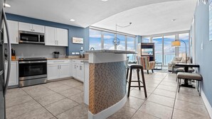 Una cocina moderna con gabinetes blancos, microondas integrado y una pared decorada con ladrillos.