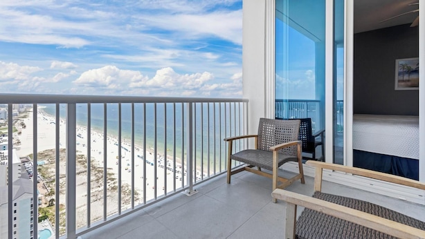 Un balcón con vista a la playa y al océano, una silla y una cama.