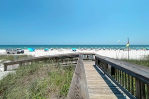 A wooden boardwalk leading to a beach with umbrellas and a flag.