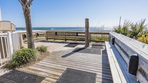 Une terrasse en bois offrant une vue sur l’océan, avec des rampes en métal et un palmier.