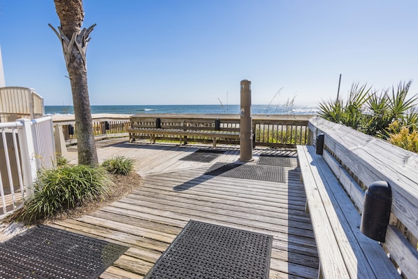 A wooden deck with a view of the ocean, metal railings, and a palm tree.