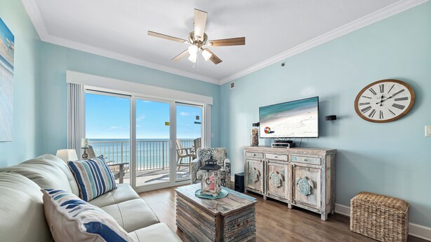 A living room with a sofa, a coffee table, a television, and a view of the ocean through large windows.