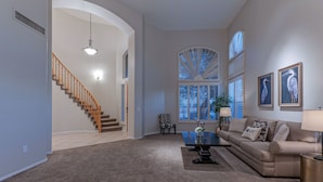 A spacious living room with a staircase, a sofa, a coffee table, and large windows with shutters. - LUX Near Golf & Trails: Pvt POOL/Spa, Wood FP, Game Tables, TVs All BRs, EV Charger (Mesa)