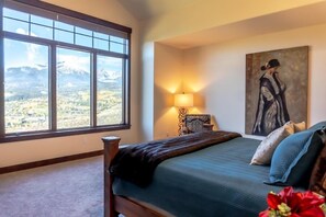 Un dormitorio con un ventanal grande, una cama, una lámpara y un cuadro.