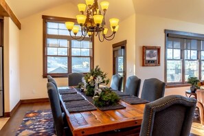 A dining room with a wooden table, chairs, a chandelier, and large windows. - Custom Home, Incredible Mountain Views, Private Hot Tub, Pool Table, Available for Monthly Rental (Silverthorne)