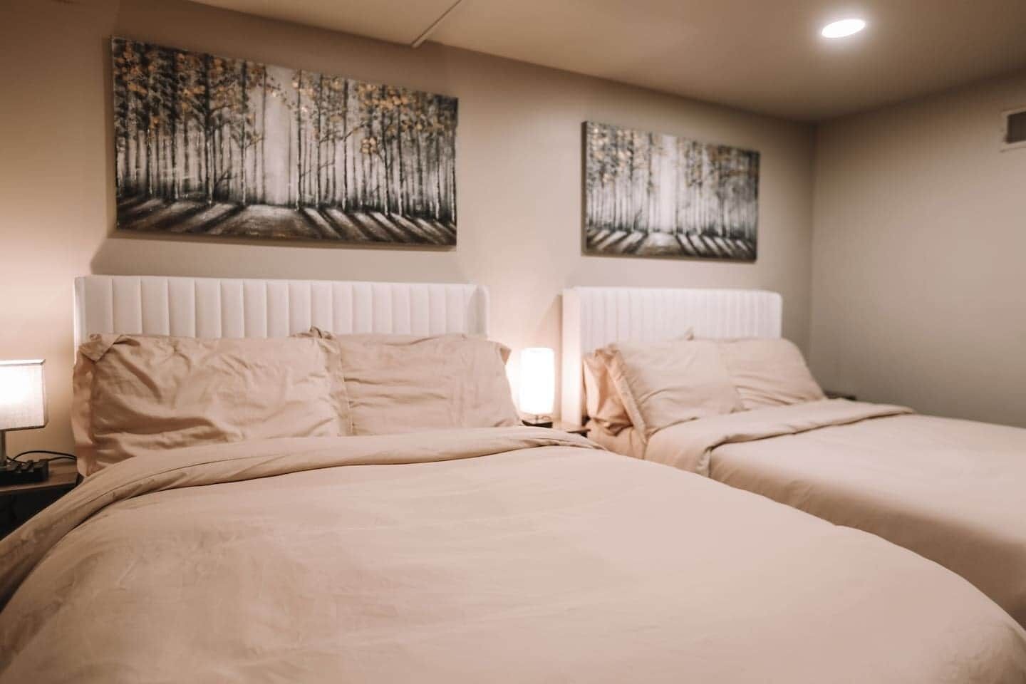 Une chambre d’hôtel avec deux lits, une table de chevet avec une lampe et deux tableaux au mur.