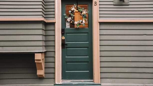 Une porte verte avec un cadre en bois, une boîte aux lettres et un panneau avec la lettre « B » au-dessus de la porte.