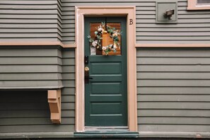 A green door with a wooden frame, a mailbox, and a 'B' sign above the door.