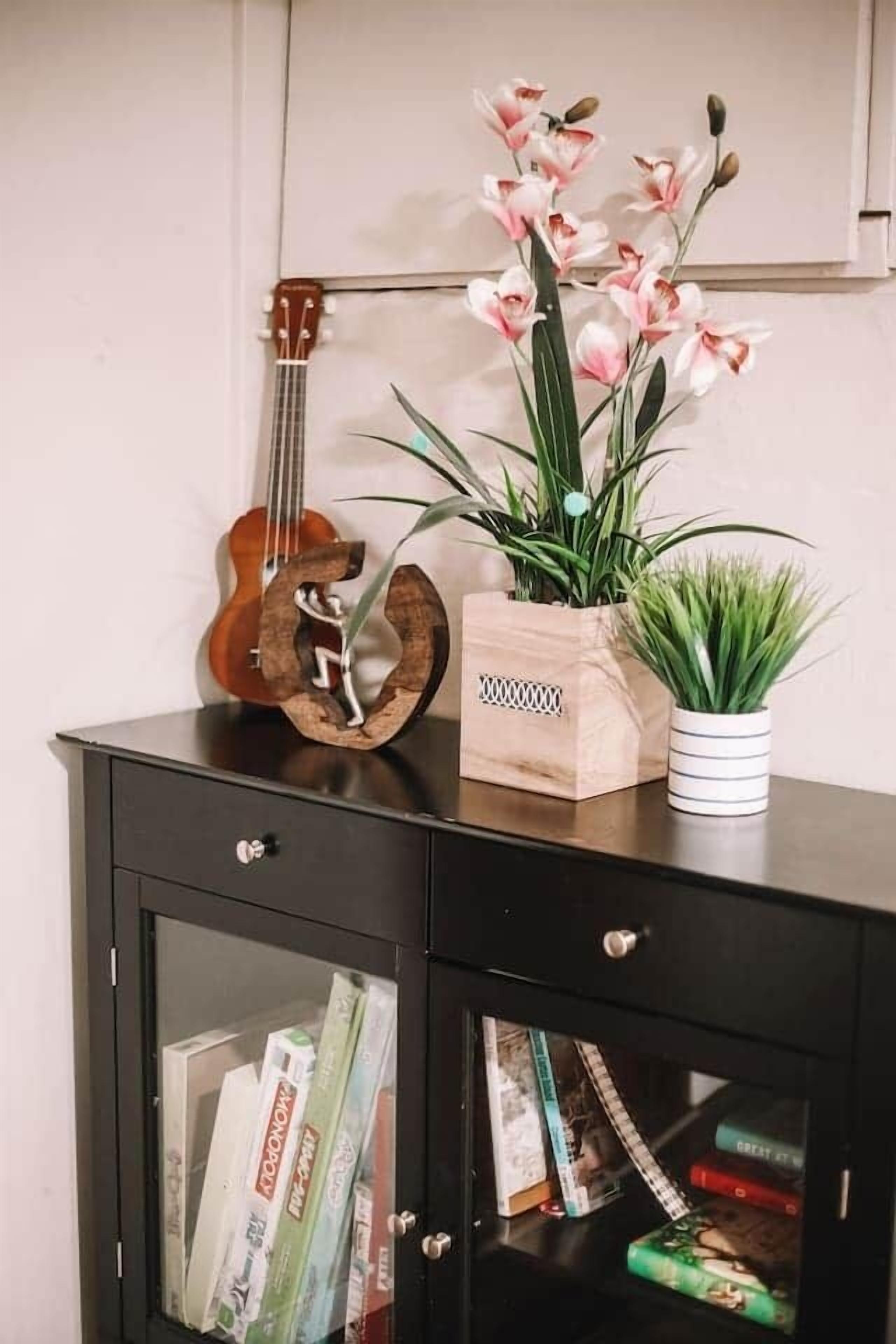 Un meuble en bois avec une guitare, un pot de fleurs en bois contenant des fleurs roses et une plante en pot.