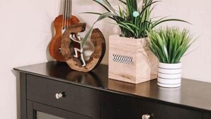 Un meuble en bois avec une guitare, un pot de fleurs en bois contenant des fleurs roses et une plante en pot.